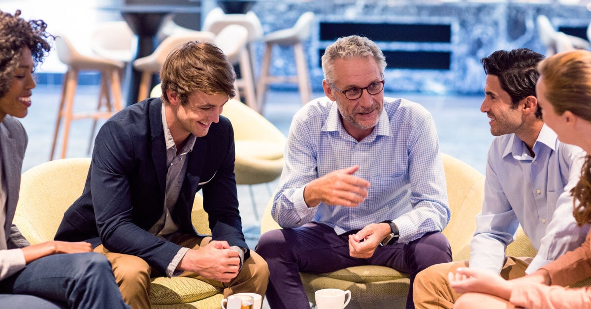 Group of colleagues sitting relaxed at coffee table listening to boss